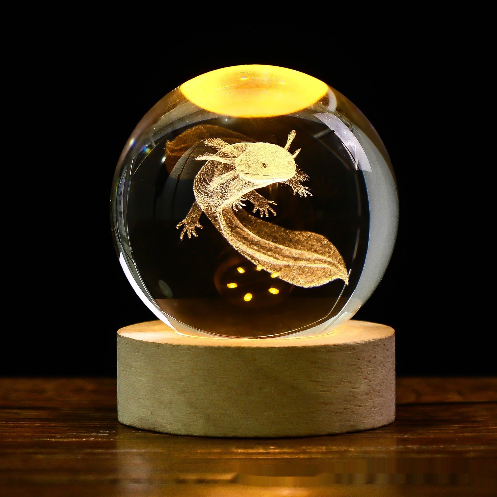 Glass sphere with a 3D laser engraving of an axolotl on a wooden base against a dark background