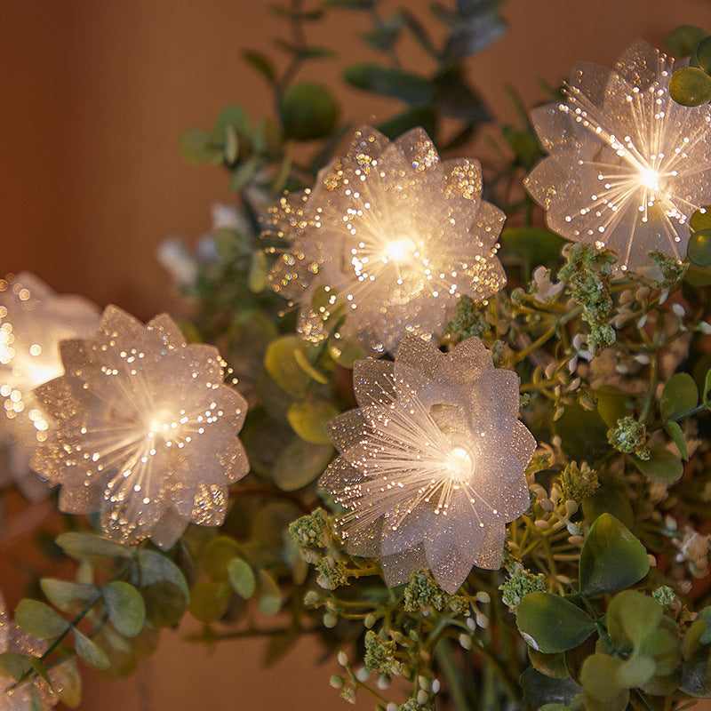 Decorative string lights shaped like flowers on a plant with a warm background