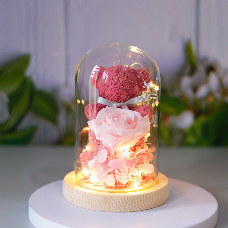 Decorative lamp with pink and red roses under a glass dome on a white surface.