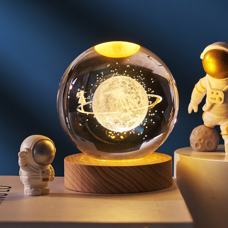 Glass ball with celestial design on a wooden base, surrounded by astronaut figurines against a dark blue background.