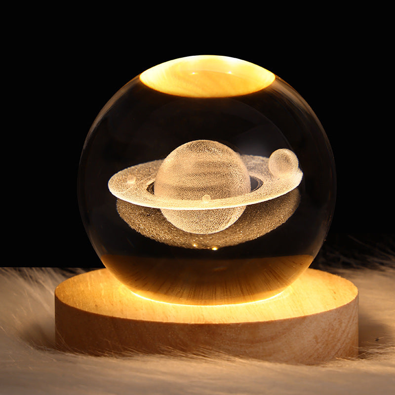 Glass sphere with a Saturn model inside on a wooden base against a dark background