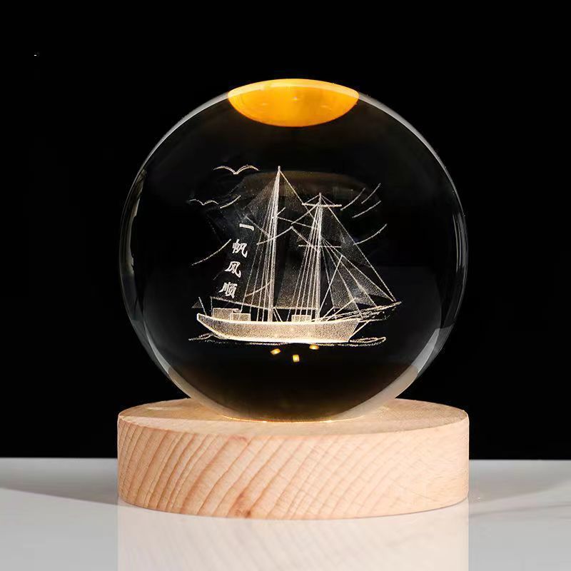 Crystal ball with ship engraving on a wooden base against a black background