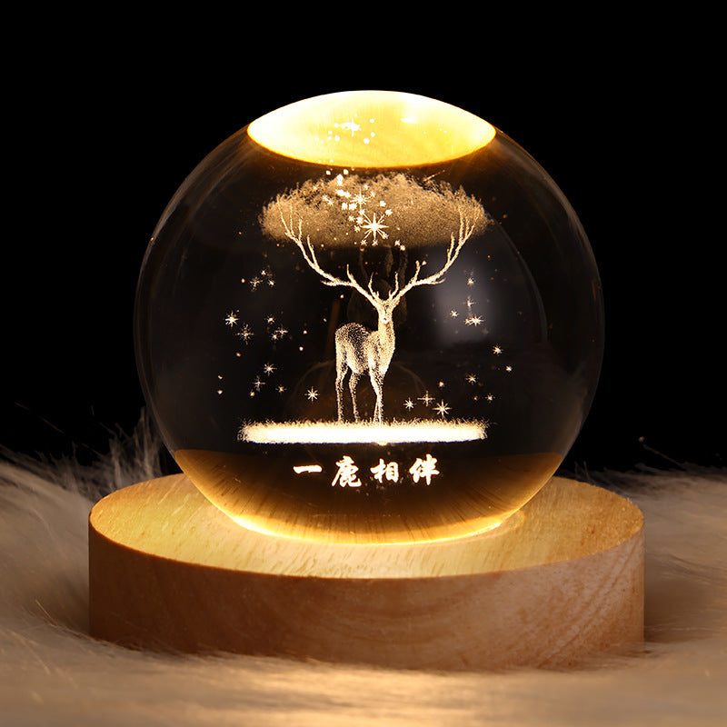 Decorative glass ball with a deer and tree design on a wooden base against a dark background